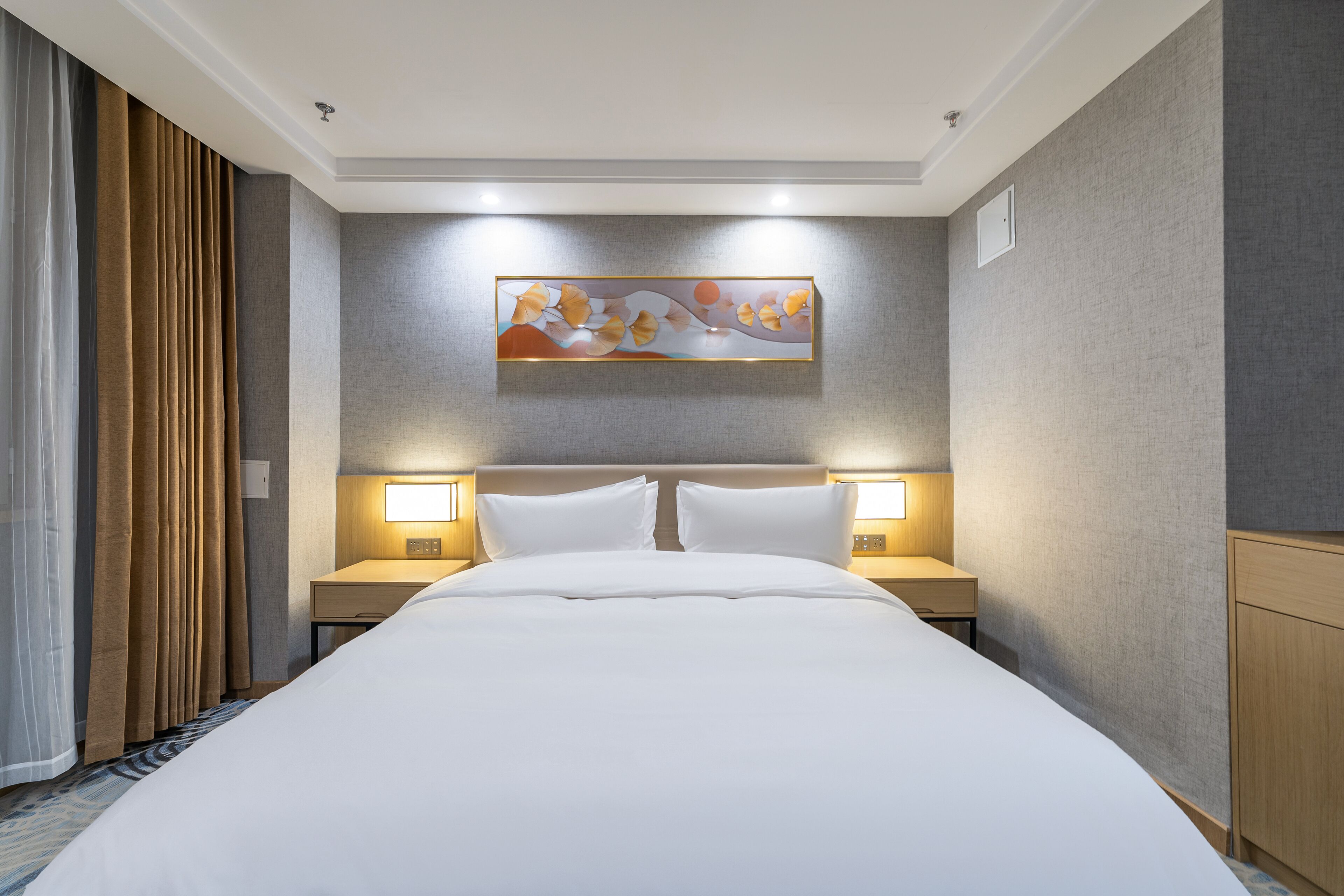 A hotel room with a large bed, two bedside tables with lamps, a headboard, and a wall-mounted artwork.