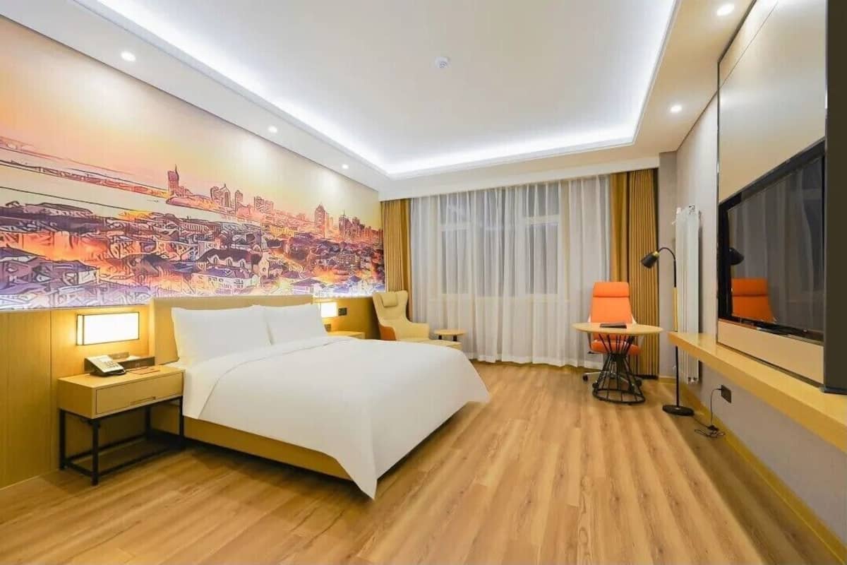 A hotel room with a bed, bedside table, lamp, chair, and a TV.