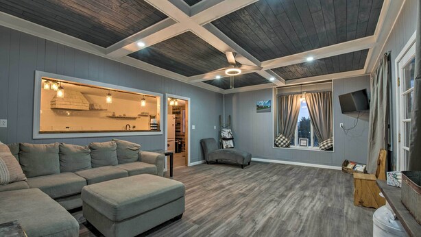 Uma sala de estar ampla com sofá seccional, teto de madeira e uma grande janela com cortinas.