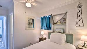 A bedroom with a bed, a nightstand, a lamp, a ceiling fan, a window with curtains, and a wall-mounted shelf with decorative items. - Ormond Beach Retreat w/ Deck - Steps to Ocean! (Ormond Beach)