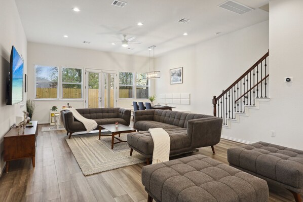 Ein großzügiges Wohnzimmer mit Ecksofa, Couchtisch und Kamin. Eine Treppe mit Geländer führt auf eine erhöhte Ebene.