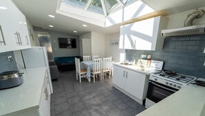 A modern kitchen with white cabinets, a gas stove, and a dining area with a table and chairs. - Studio Close to University of Birmingham (Birmingham)