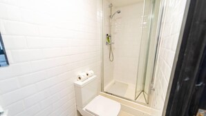 A small, white-walled bathroom with a toilet, a shower with a glass door, and a toilet paper holder. - Studio Close to University of Birmingham (Birmingham)
