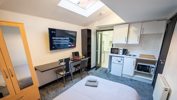A compact hotel room with a bed, a desk, a TV, a kitchenette, and a wardrobe. - Studio Close to University of Birmingham (Birmingham)