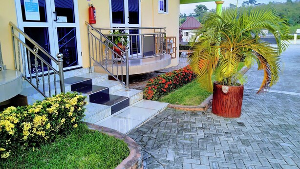 A building with a staircase leading to a covered entrance, a fire extinguisher mounted on the wall, and a potted palm tree. - Renajoe Ejisu-Kubease (Kubease)