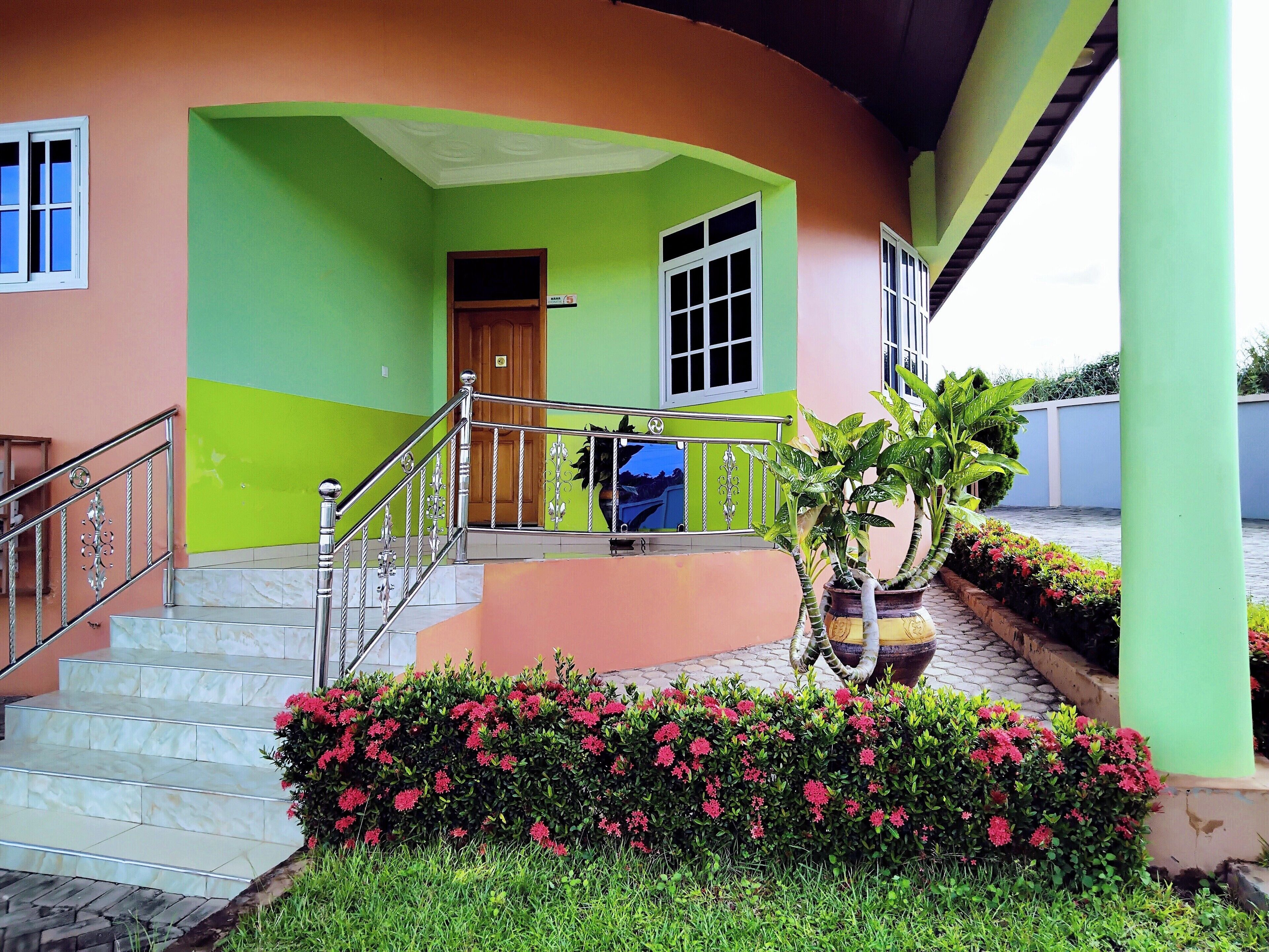 Ein Gebäude mit einer Fassade in Grün und Orange, eine Treppe, die zu einer Tür führt, und ein Blumentopf mit rosa Blüten.