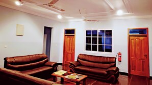 A living room with two leather sofas, a coffee table, a ceiling fan, and a window with blinds. - Renajoe Ejisu-Kubease (Kubease)