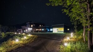 Una casa moderna de noche con un camino de entrada que lleva a la puerta.