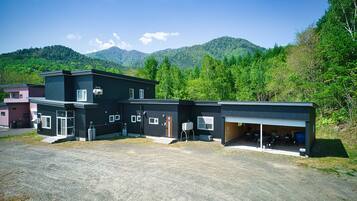 A modern building with a garage and outdoor seating area, surrounded by lush greenery and mountains.