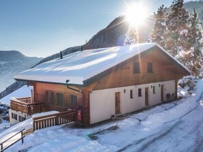 A wooden cabin with a snow-covered roof, a wooden deck, and a mountain backdrop. - Plein Sud 3 by Interhome (Ovronnaz)