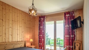 A wooden-paneled room with a bed, a TV mounted on the wall, and a window with red curtains. - Plein Sud 3 by Interhome (Ovronnaz)