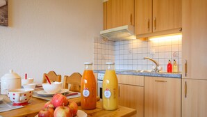 A kitchen with wooden cabinets, a tiled backsplash, and a wooden table with a plate of apples and two bottles of juice. - Plein Sud 3 by Interhome (Ovronnaz)