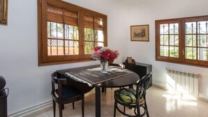 Un área de comedor con una mesa, sillas, un florero y ventanas grandes con marcos de madera.