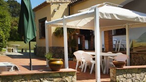 Un patio con toldo blanco, paredes de piedra y mobiliario exterior.