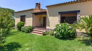 Una casa de dos plantas con techo de tejas, una chimenea y un pequeño porche con escalones que conducen a la entrada.