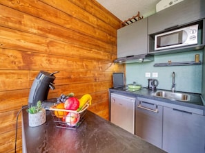 Une cuisine de taille réduite avec des murs en bois, un four à micro-ondes, un évier et un panier de fruits posé sur le plan de travail.