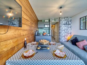 Un salon chaleureux avec un mur en bois, une table à manger dressée pour le repas et un canapé agrémenté de coussins.