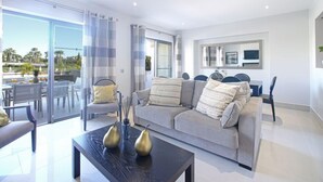 A modern living room with a grey sofa, a coffee table with decorative vases, and a dining area with a glass door leading to an outdoor patio.