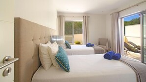 A hotel room with two beds, a chair, and a balcony with sun loungers.