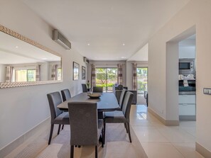 Un espace repas moderne, doté d’une grande table, de chaises et offrant une vue sur l’extérieur.