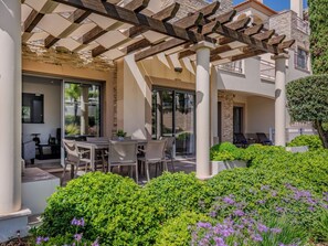 A covered outdoor seating area with a table and chairs, surrounded by lush greenery and flowering plants. - Pine Hills Ametista by Interhome (Vilamoura)