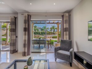 A modern living room with a glass door leading to an outdoor patio, a grey armchair, and a glass coffee table.