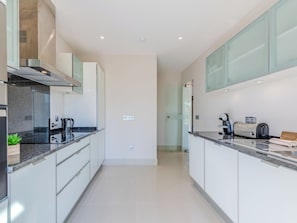 A modern kitchen with white cabinetry, a stainless steel range hood, and a countertop with a coffee maker and toaster. - Pine Hills Rubi by Interhome (Vilamoura)