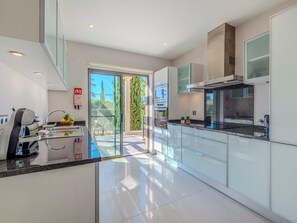 Una cocina moderna con una isla grande, electrodomésticos integrados y un ventanal corredero a un espacio exterior.