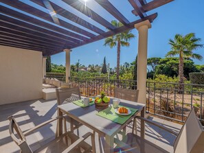 Eine Terrasse im Freien mit einem für das Frühstück gedeckten Tisch, umgeben von einem Metallzaun und Palmen.