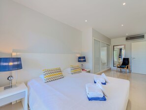 A modern hotel room with a large bed, two bedside lamps, a chair, and a door leading to a bathroom. - Pine Hills Rubi by Interhome (Vilamoura)