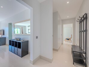 A modern interior with a hallway leading to a door, a black console table with a decorative bowl, a mirror with a patterned frame, and a metal rack with hooks. - Pine Hills Rubi by Interhome (Vilamoura)