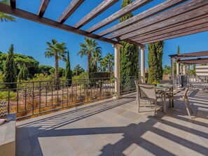 An outdoor patio with a pergola, seating, and a view of palm trees and cypress trees. - Pine Hills Rubi by Interhome (Vilamoura)
