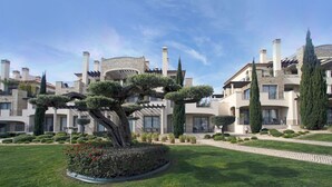 A well-maintained garden with a large, uniquely shaped tree in the center, surrounded by neatly trimmed hedges and a variety of shrubs. - Pine Hills Pérola by Interhome (Vilamoura)
