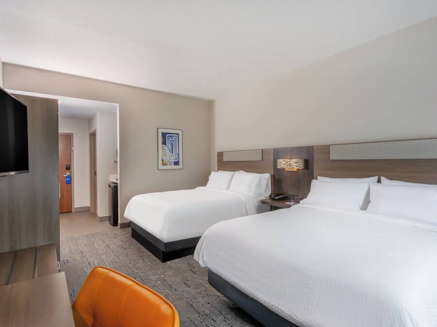 A hotel room with two beds, a TV, a desk, and a chair.