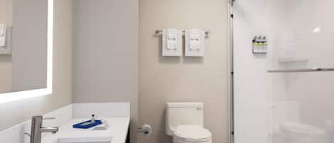 Een moderne badkamer met een witte wastafel, toilet en douche. Boven het toilet hangen twee handdoeken aan een rek.