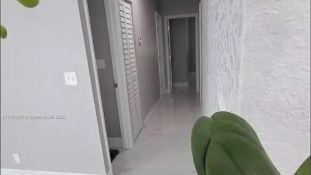 Un couloir doté d’un sol en marbre blanc, d’une plante en pot et d’orchidées blanches.