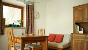A dining area with a wooden table and chairs, a sofa with a cushion, a clock on the wall, and a window with curtains. - THE BOZZLE, THE COMBA of Aosta (Valle d'Aosta)