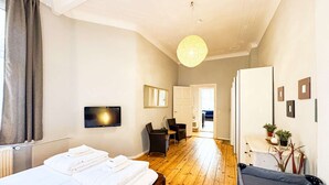 A hotel room with a wooden floor, a bed with white linens, a desk with a chair, a hanging light fixture, and a door leading to another room. - primeflats - Apartment Kattegat Berlin-Wedding (Berlin)
