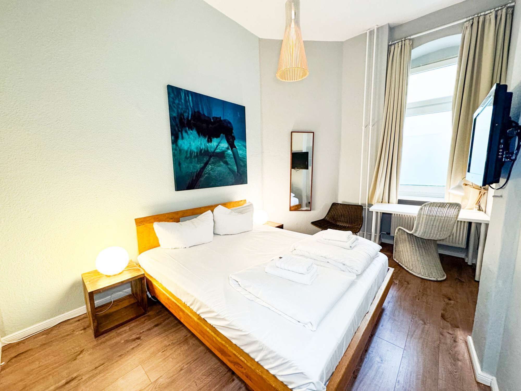 A hotel room with a large bed, a desk, a chair, a TV, and a painting on the wall.