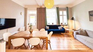 A modern living room with a wooden dining table, sofas, and a TV mounted on the wall. - primeflats - Apartment Kattegat Berlin-Wedding (Berlin)