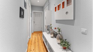 A hallway with a wooden floor, white walls, a white door, and a white console table with decorative items. - primeflats - Apartment Kattegat Berlin-Wedding (Berlin)