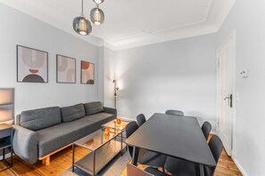 En moderne stue med en grå sofa, et glasbord, et spisebord med stole og tre pendellamper monteret på væggen.