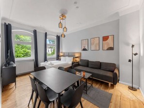 Ein modernes Hotelzimmer mit einem Bett, einer Couch, einem Esstisch mit Stühlen, einer Stehlampe und Kunstwerken an der Wand.