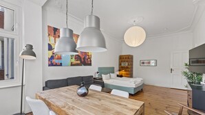 Una habitación de hotel moderna con zona de comedor, cama, sofá y un cuadro grande en la pared.