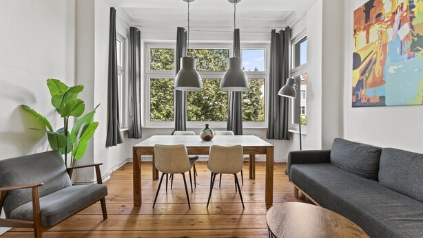 Una sala de estar moderna con una mesa de comedor, dos sillas, un sofá y un ventanal con cortinas.