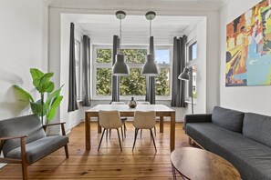 Una sala de estar moderna con una mesa de comedor, dos sillas, un sofá y un ventanal con cortinas.