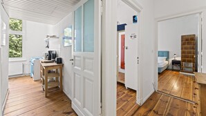 Una habitación con piso de madera, una cama con cabecera azul, un armario de madera y una puerta que da a otra habitación.