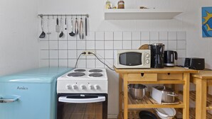 Una cocina compacta con estufa Amica, microondas, cafetera y estante de madera con ollas.