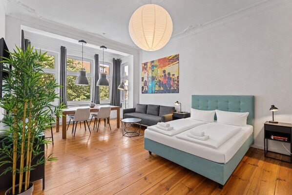 A modern hotel room with a bed, a dining area, a large window, and a hanging light fixture.