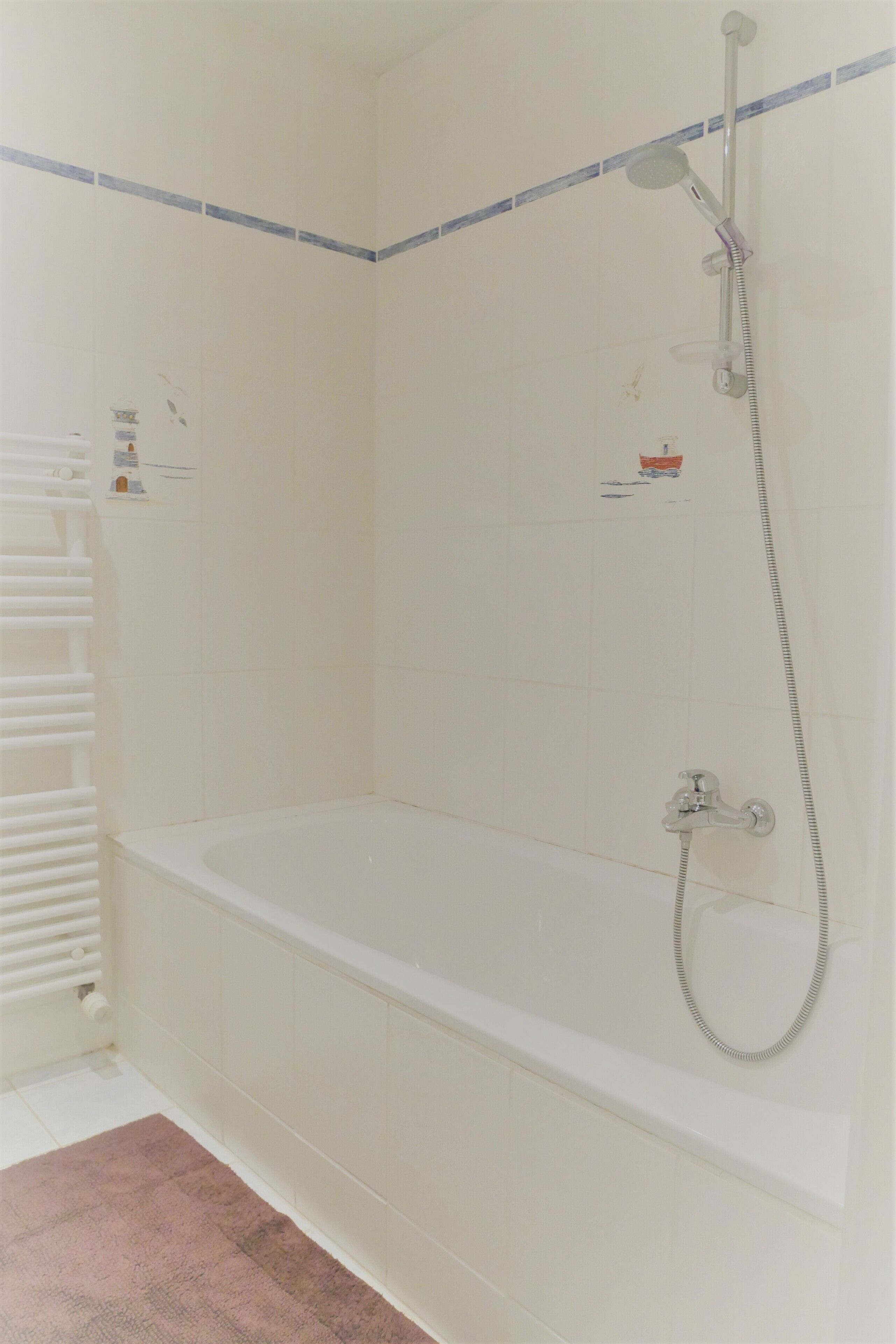 Une salle de bain blanche avec une baignoire, une pomme de douche et un porte-serviettes.